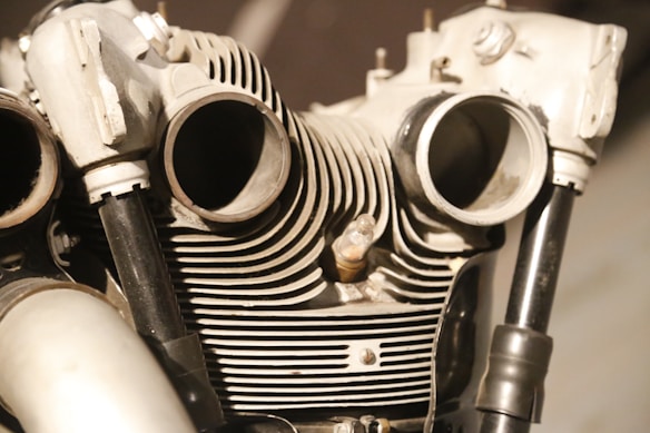 An intricate view of a mechanical engine, showcasing cylinder heads and cooling fins in close detail. The image highlights the metallic textures and complex shapes, with prominent pipes and bolt details.