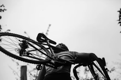 greyscale photography of man carrying bike
