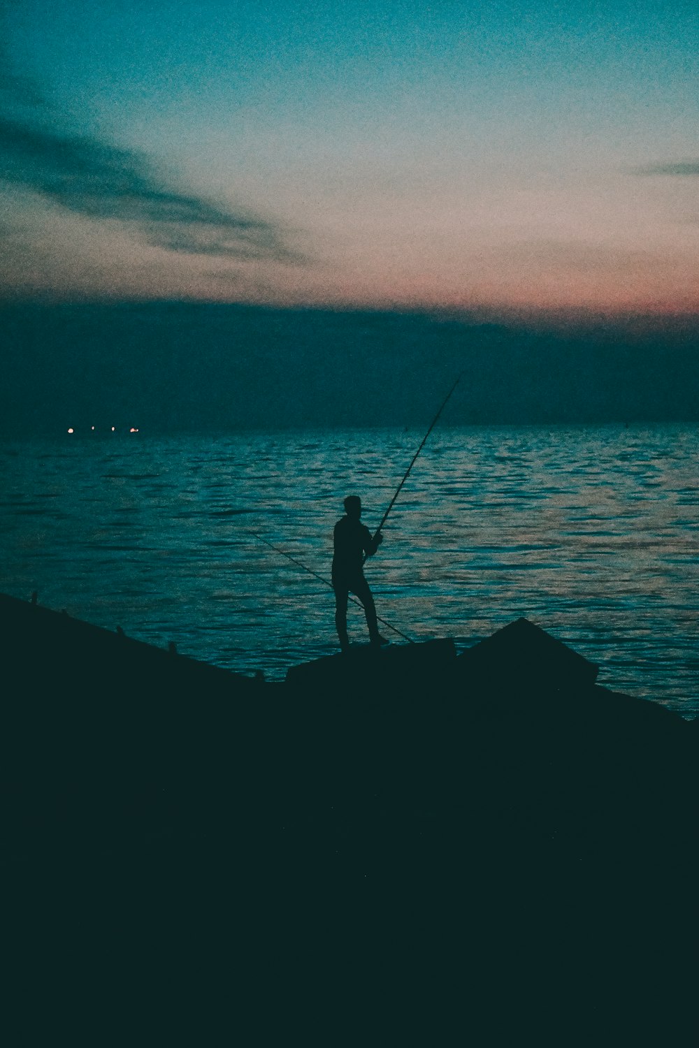 silhouette of person fishing across body of water