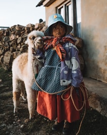 girl wearing multicolored dress standing near white llama