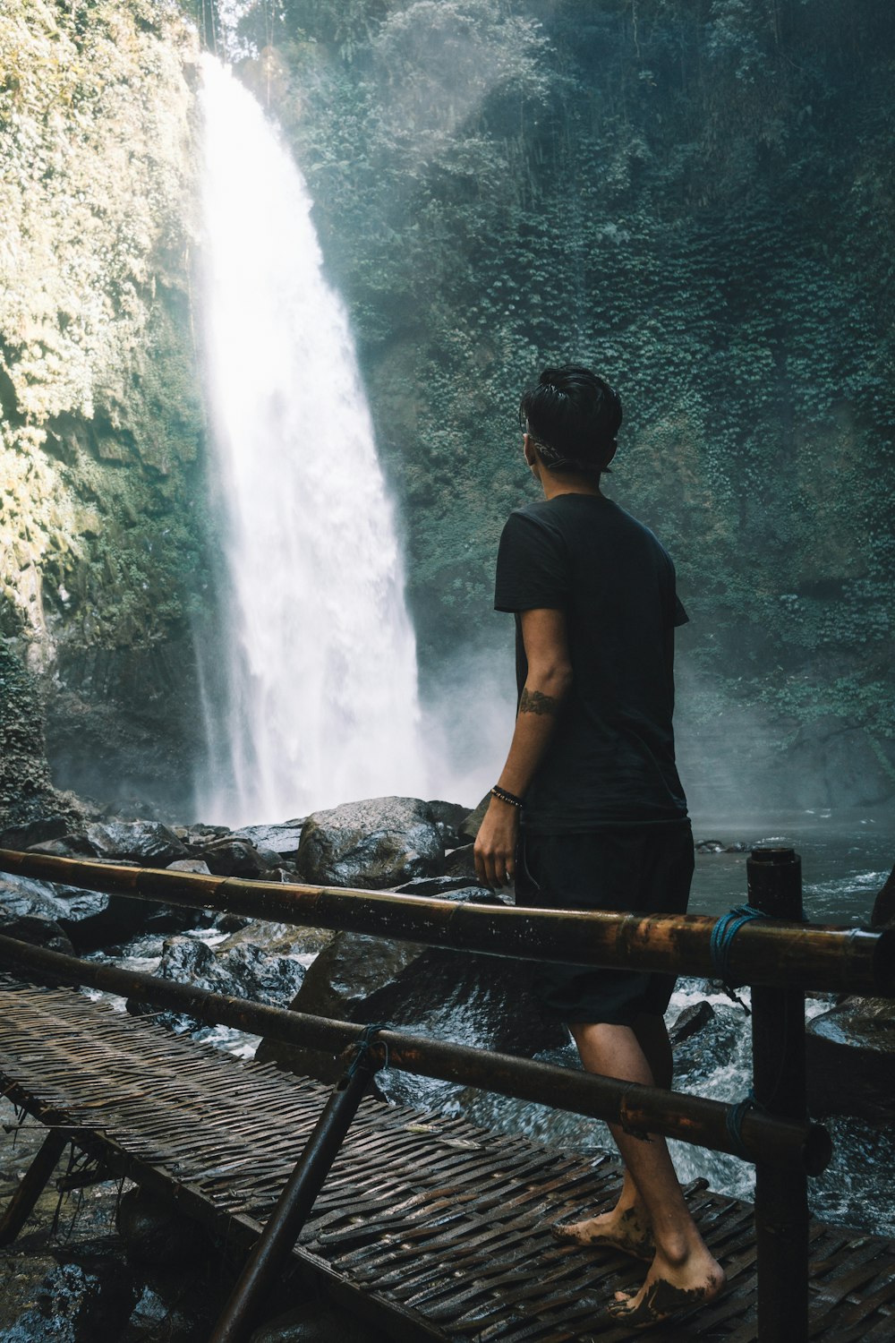 man wearing black crew-neck shirt walking on brown bridge