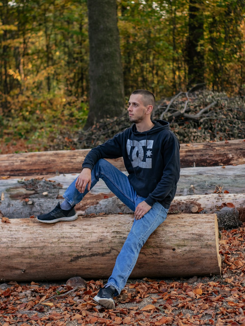 man wearing black DC hooded jacket and blue denim jeans sitting on brown log