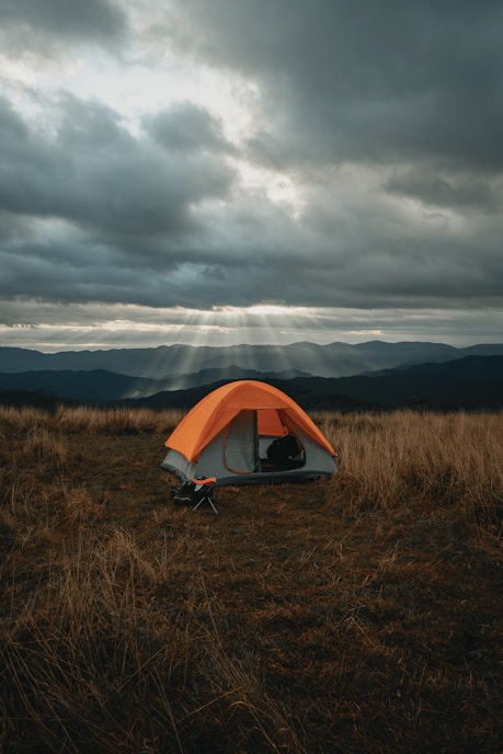 set-up gray and orange tent on brown field under cloudy sky