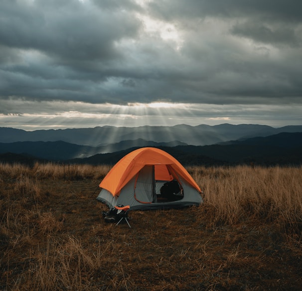 set-up gray and orange tent on brown field under cloudy sky