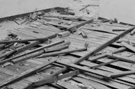 Broken wooden floorboards and scattered debris cover the ground in an indoor space. The floor appears damaged with displaced panels and exposed nails, giving an impression of neglect or abandonment.