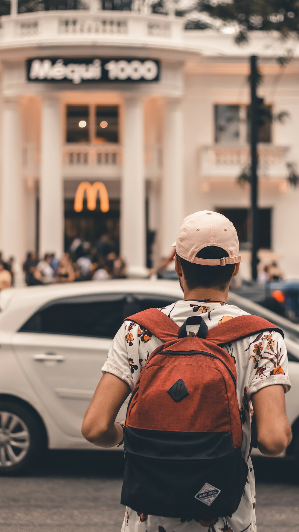 man wearing floral shirt carrying backpack beside road