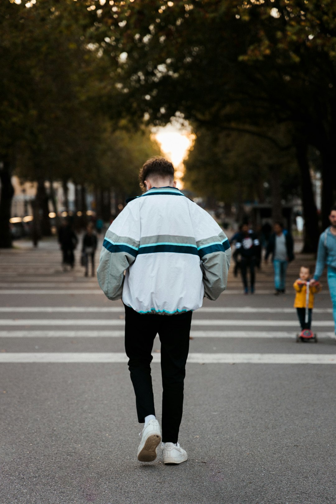 man wearing white and blue jacket and black jeans walking on street