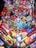A colorful pinball machine playfield features a comic book theme with various superhero characters and villains, including a prominent red-masked figure at the top center. There are vibrant illustrations of characters like Juggernaut, Mystique, and others, surrounded by dynamic comic-style text and vibrant graphics. The playfield includes various ramps, targets, and lanes decorated with red, blue, yellow, and green shades.