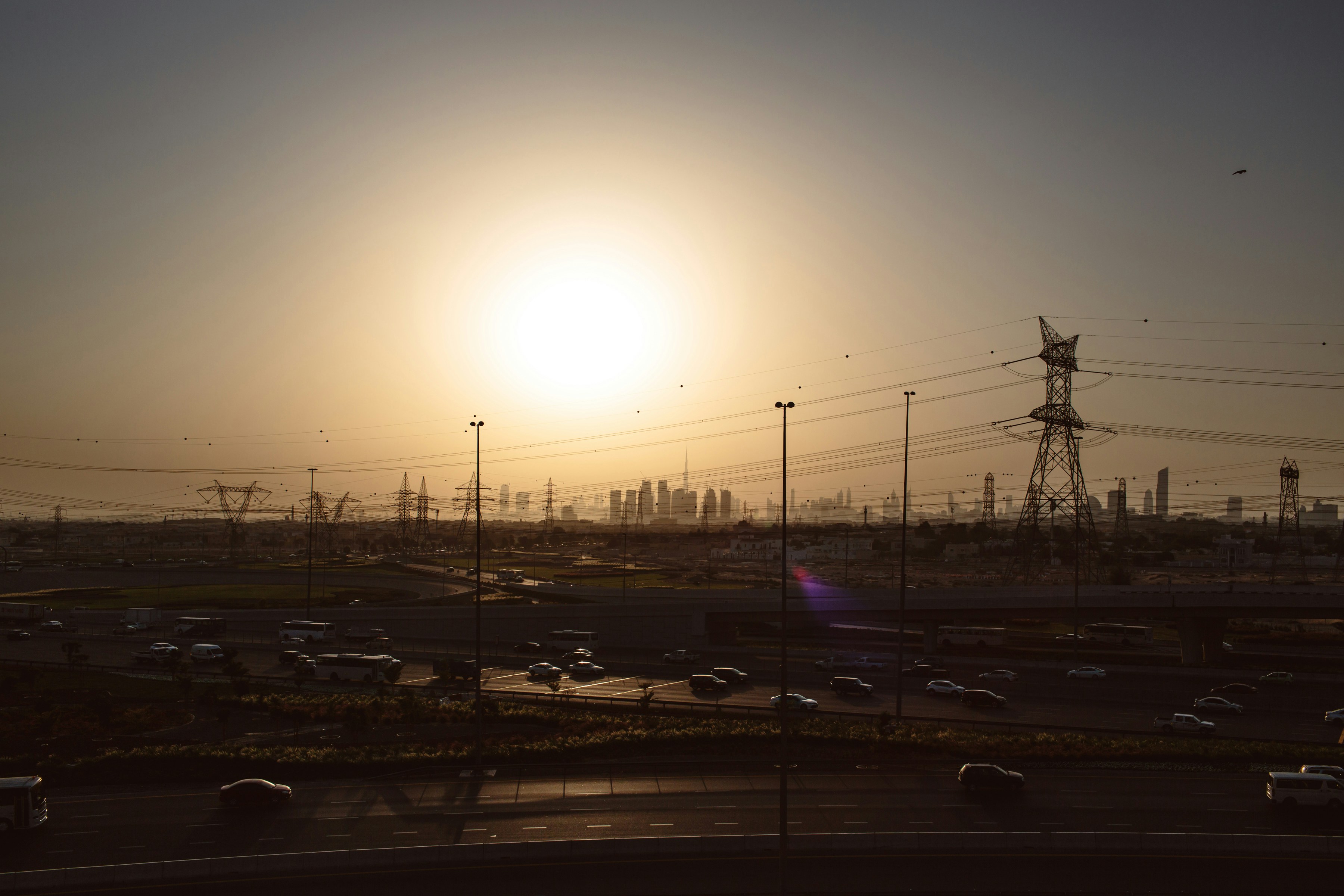 The sun sets over the Dubai outskirts, as the Burj Khalifa and city skyline rise in the far background.