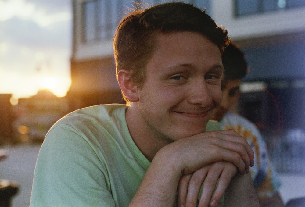 smiling man in green crew-neck shirt near building