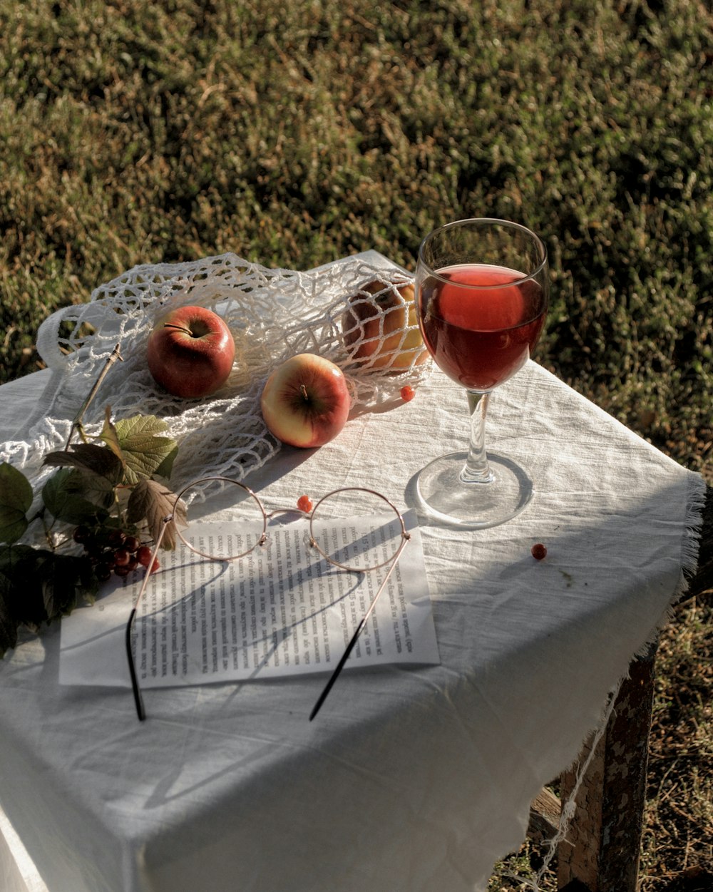 glass of red wine near three apple fruits on table