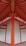 A detailed architectural view of a structure with vibrant orange beams and white panels, forming a symmetrical and geometric pattern. The beams converge at the ceiling, creating a striking visual impact with clean lines and a modern design.