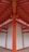 A detailed architectural view of a structure with vibrant orange beams and white panels, forming a symmetrical and geometric pattern. The beams converge at the ceiling, creating a striking visual impact with clean lines and a modern design.