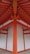 A detailed architectural view of a structure with vibrant orange beams and white panels, forming a symmetrical and geometric pattern. The beams converge at the ceiling, creating a striking visual impact with clean lines and a modern design.