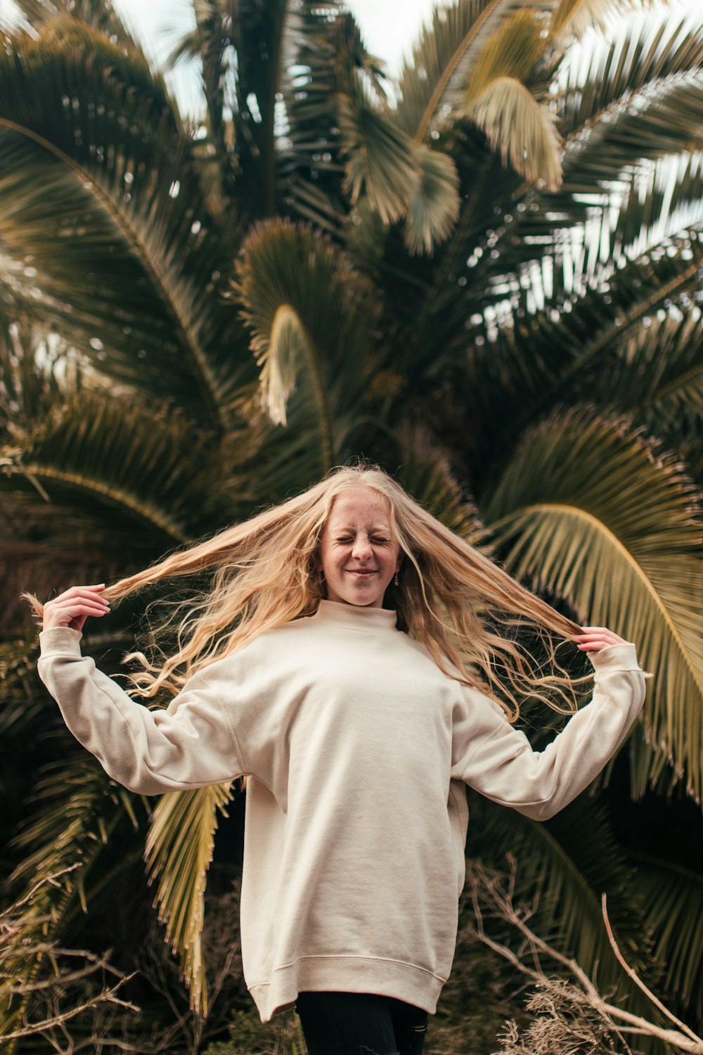 woman smiling and touching her hair in front of tree during day