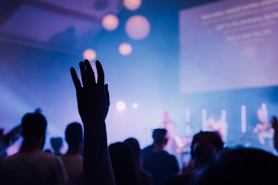 A cinematic wide-angle view of a live music event with an intimate crowd, illuminated by subtle blue and wine lighting.