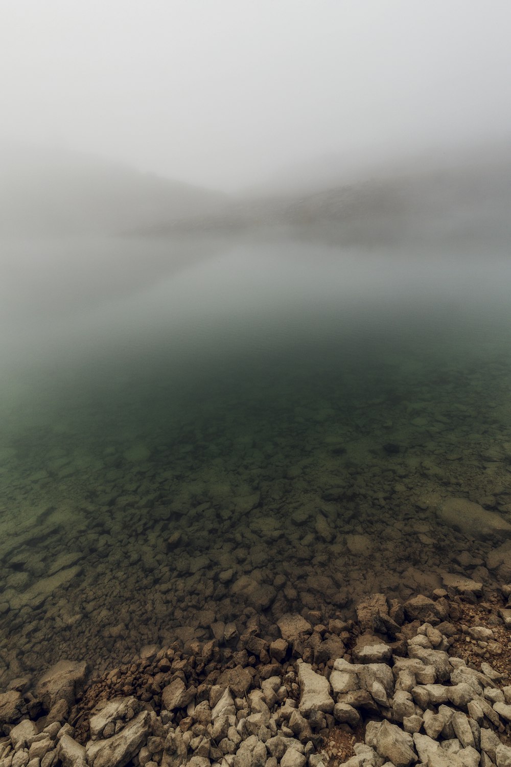 a body of water surrounded by rocks and fog