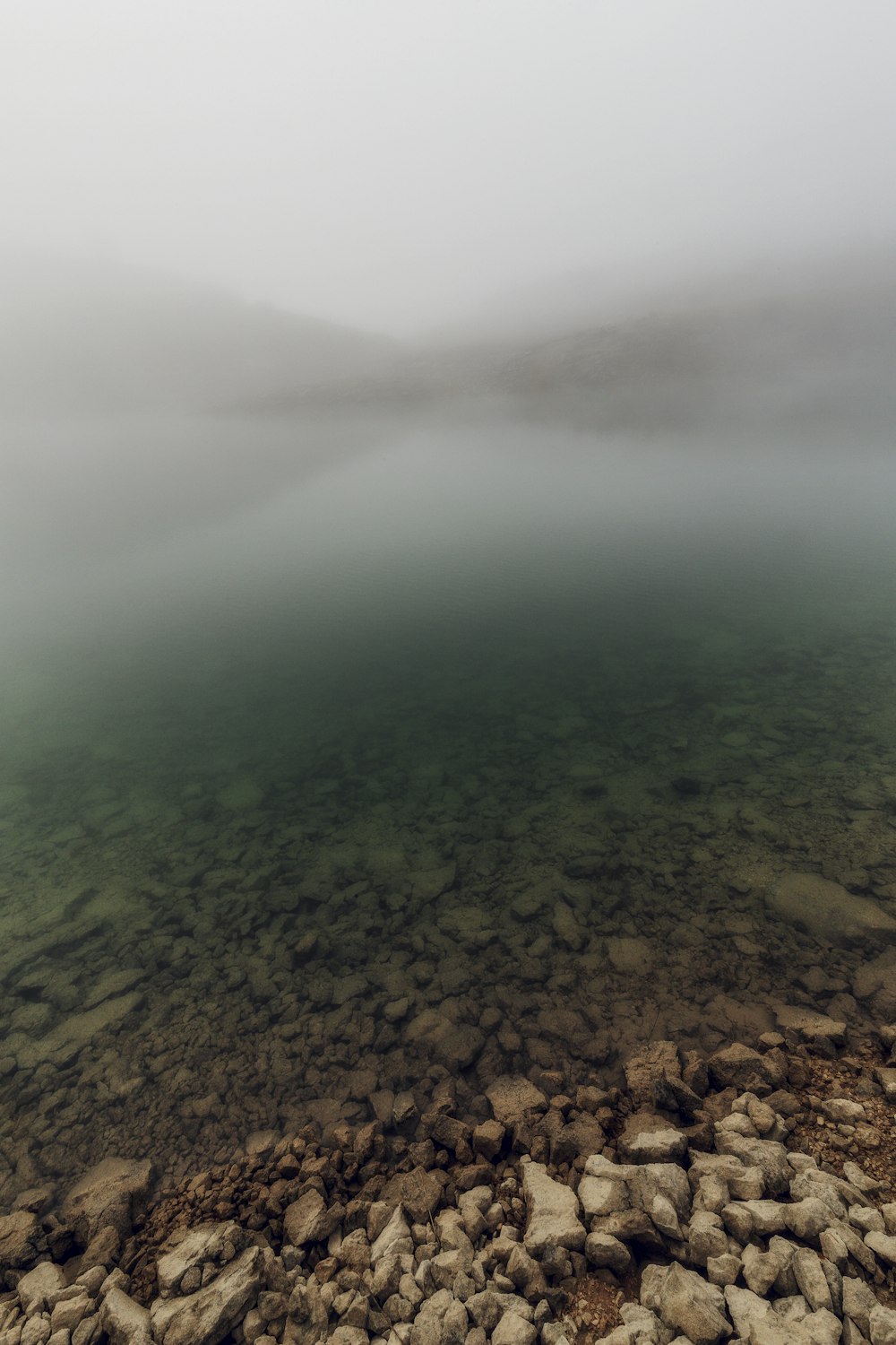 ein Gewässer, umgeben von Felsen und Nebel