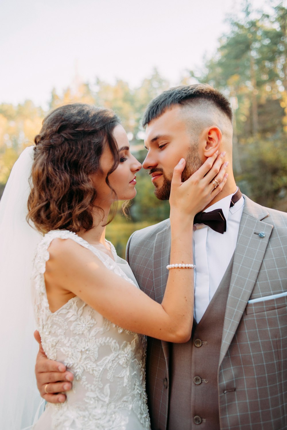 Frau im Brautkleid hält das rechte Kinn eines Mannes, beide sind im Begriff, sich zu küssen