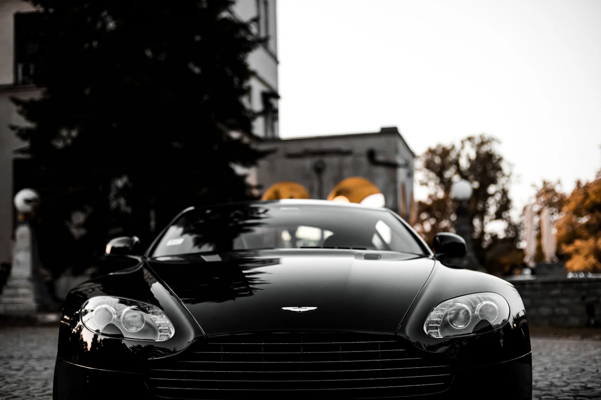 A sleek black luxury car with a mirror-like shine parked in an elegant urban setting at dusk.