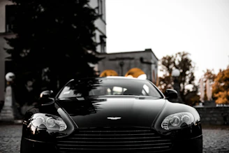 A sleek black luxury car with a mirror-like shine parked in an elegant urban setting at dusk.