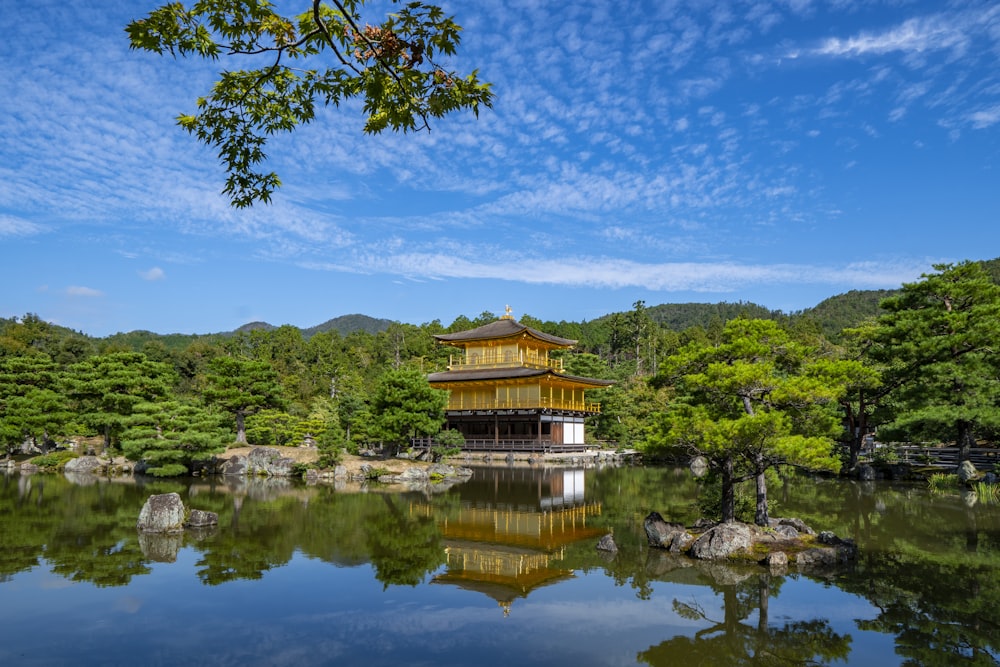 日本の金閣寺は、昼間は青と白の空の下、水域の近くにある背の高い緑の木々に囲まれています