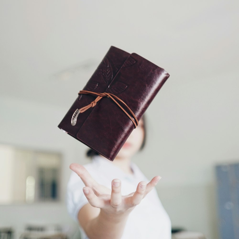 brown leather clutch wallet in mid air above woman's hand