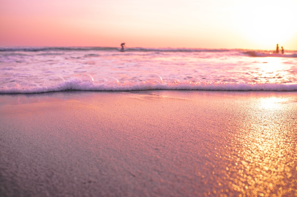 three persons in sea during golden hour