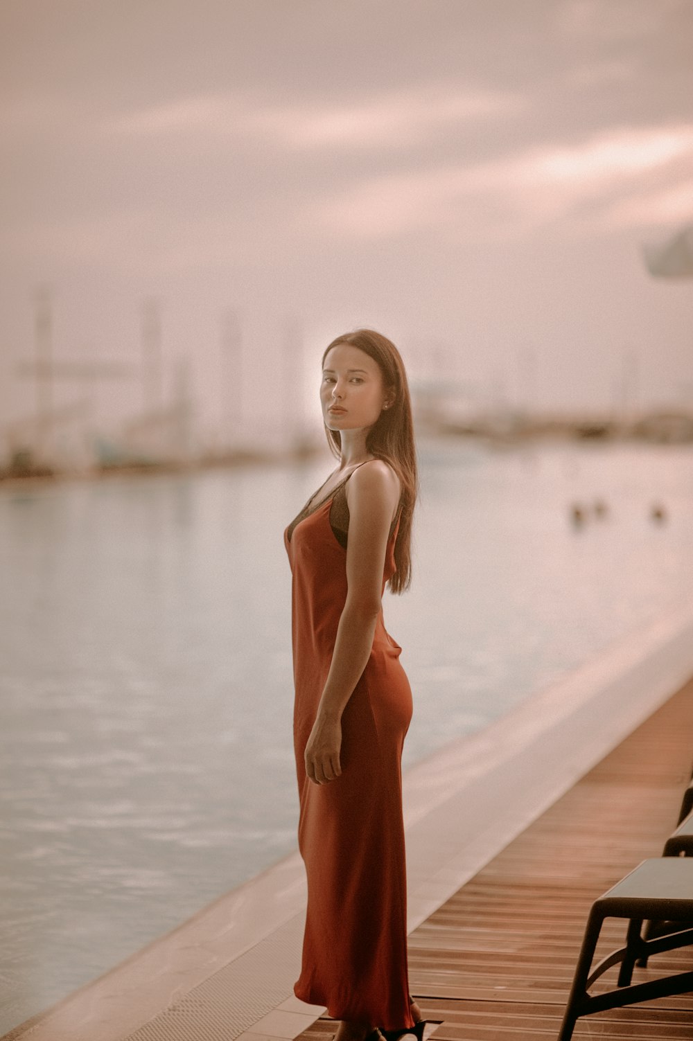 woman wearing orange sleeveless dress standing near body of water during daytime