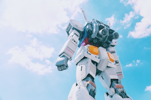 The silhouette of a Gundam model, staring into a cloudy blue sky.