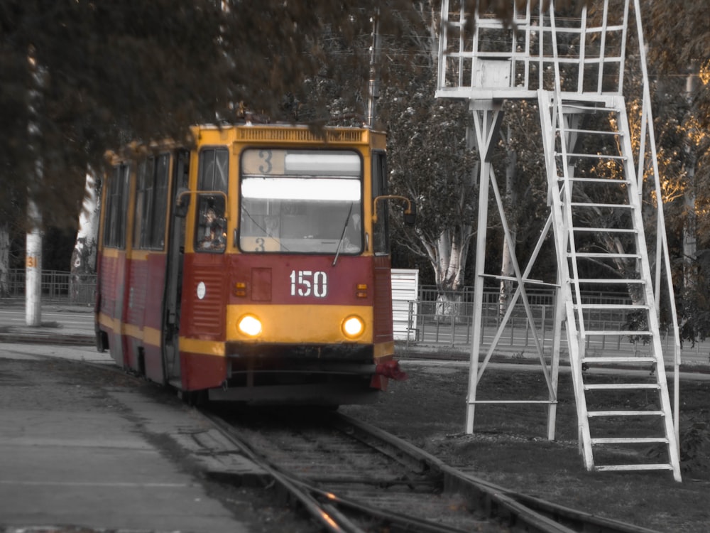 yellow and red tram surrounded with tall and green trees during daytime