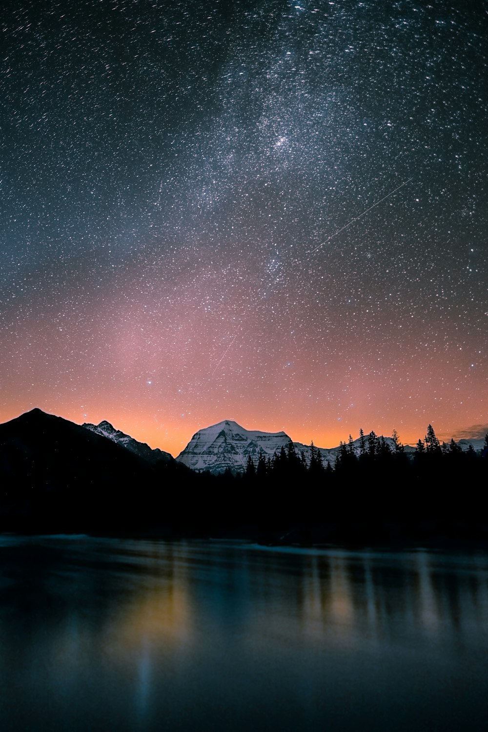 lake surrounded by trees and mountain under milky way