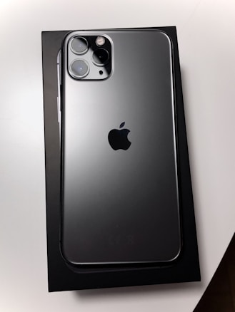 A sleek smartphone with a metallic finish is placed on top of its box. The back showcases three camera lenses and the iconic logo in the center, highlighting its premium design.