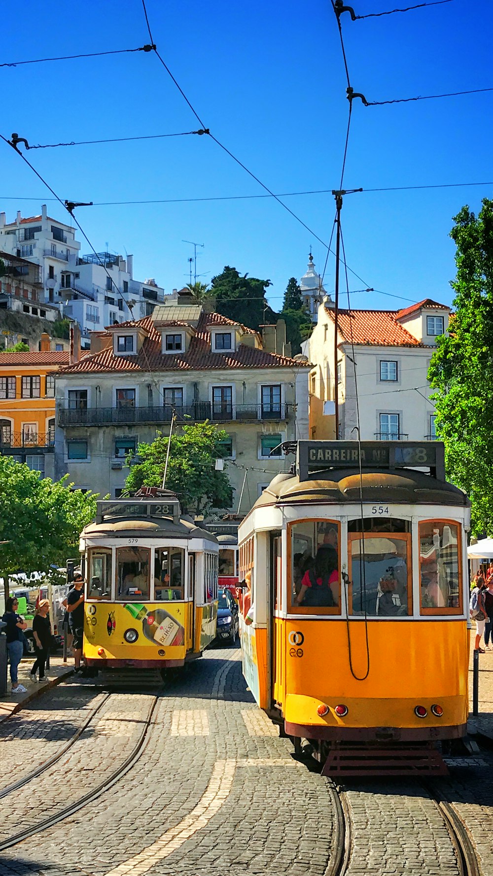 people inside yellow tram and others are standing near road during daytime