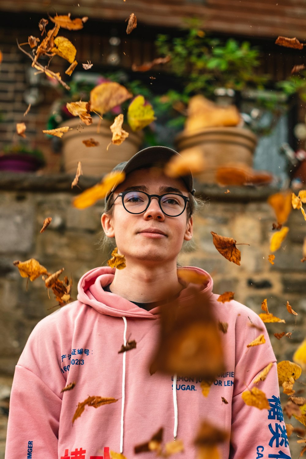 man wearing pink pullover hoodie and grey cap with dried leaves falling