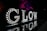 Illuminated letters spelling out 'GLOW' are displayed against a dark background. Each letter is adorned with bright lights, and the reflection of the letters can be seen on a shiny surface below. In the background, trees are illuminated with vibrant purple and red lights.