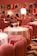 A stylish dining area with plush pink chairs and white tablecloths, elegantly arranged with gold lamps on each table. The ambient lighting creates a warm and inviting atmosphere. The walls are adorned with modern art prints, adding a contemporary flair to the decor. Diners can be seen in the background, engaged in conversation.