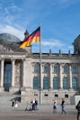 people walking beside building with waving flag of Germany on pole