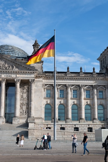 people walking beside building with waving flag of Germany on pole