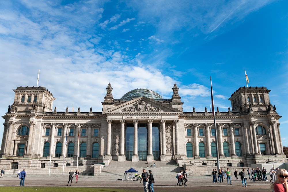 Menschenmenge geht und sitzt tagsüber vor einem grauen Betongebäude