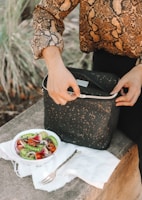 woman opening lunch bag near bowl of salad