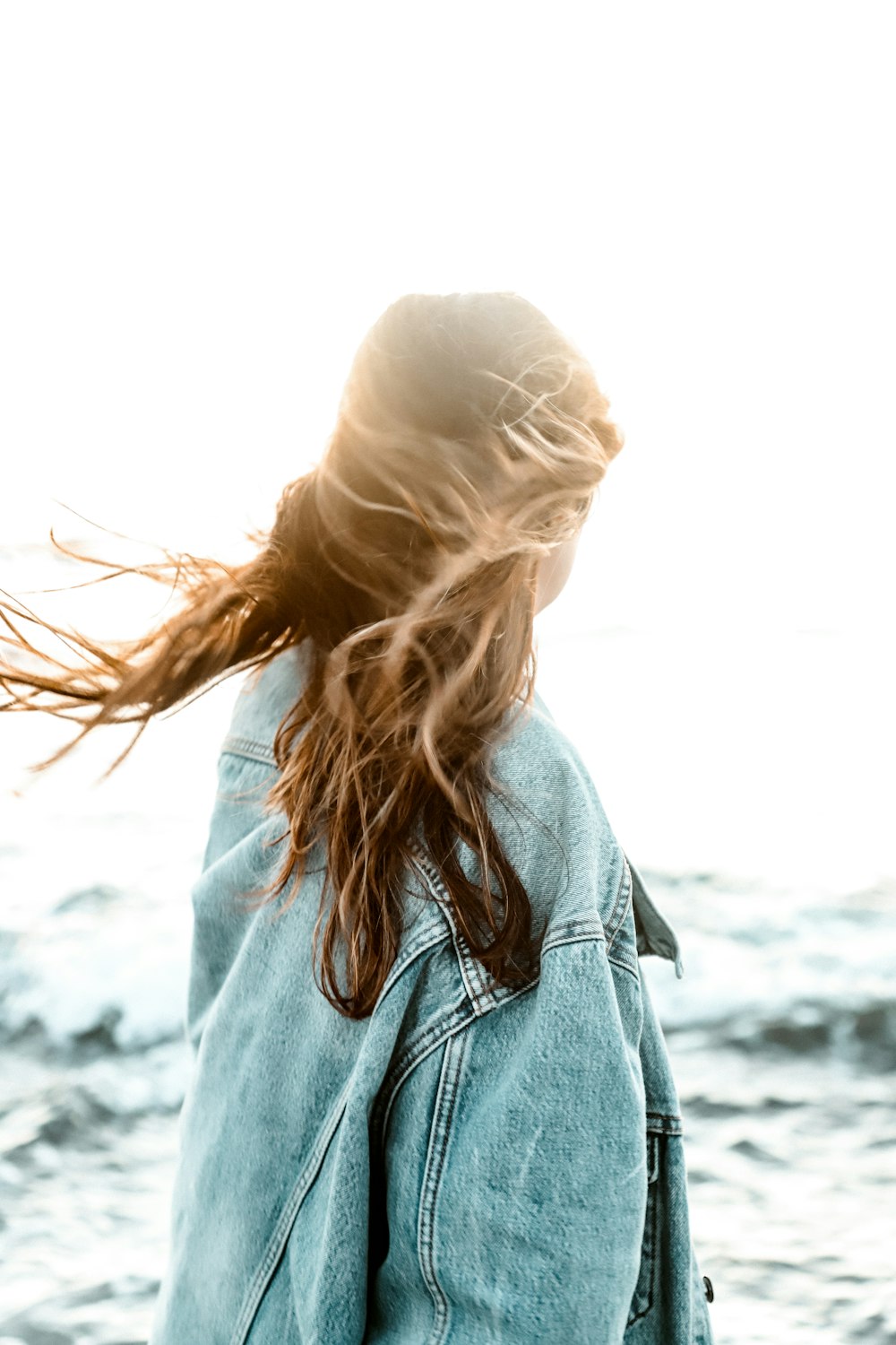 woman wearing blue denim jacket facing the body of water