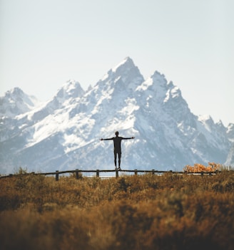 man standing on fence overlooking mountain range