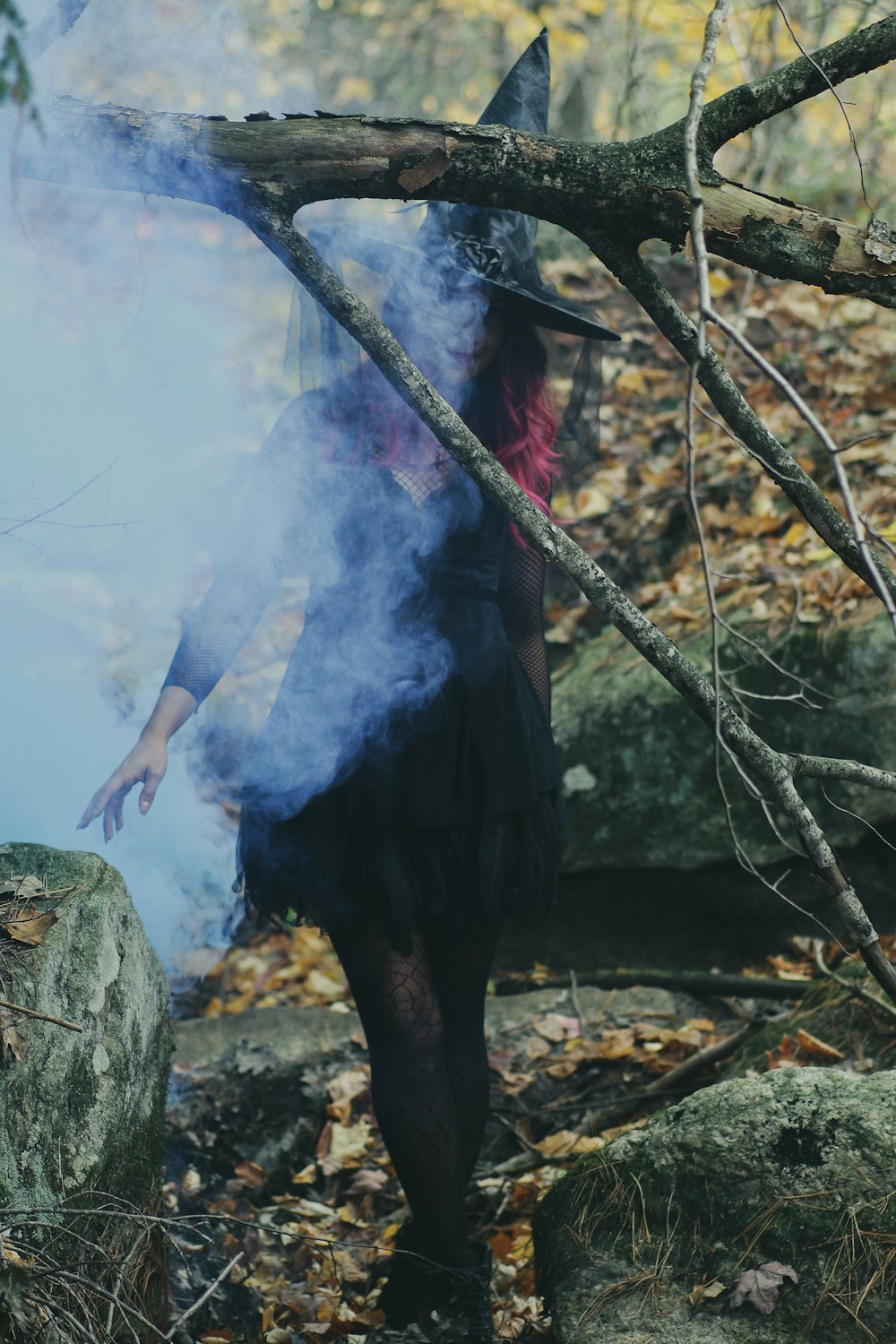Mujer en traje de bruja de pie junto a la roca
