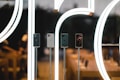A display of four sleek smartphones positioned in front of a large, illuminated logo inside a modern store. The background is softly blurred, showcasing wooden tables with more electronic devices and warm lighting.