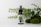 A small glass bottle with a spray nozzle labeled 'Pharma Hemp' is placed in front of a backdrop of green leaves and mossy stones on a white surface.