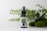 A small glass bottle with a spray nozzle labeled 'Pharma Hemp' is placed in front of a backdrop of green leaves and mossy stones on a white surface.