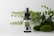 A small glass bottle with a spray nozzle labeled 'Pharma Hemp' is placed in front of a backdrop of green leaves and mossy stones on a white surface.