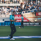 man walking and holding ball near man and people at the bleachers