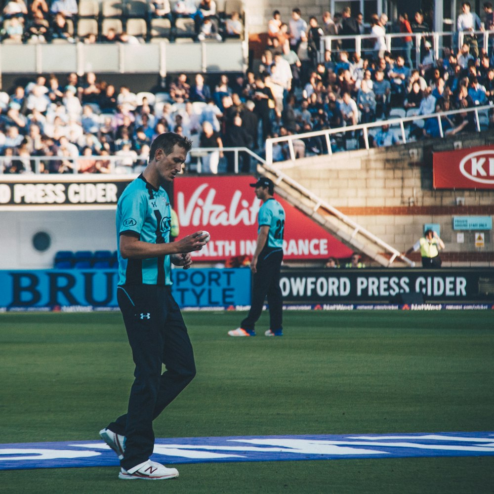 man walking and holding ball near man and people at the bleachers